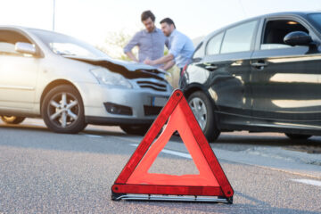 emergency sign with a car accident with two men with collision insurance in california in the back