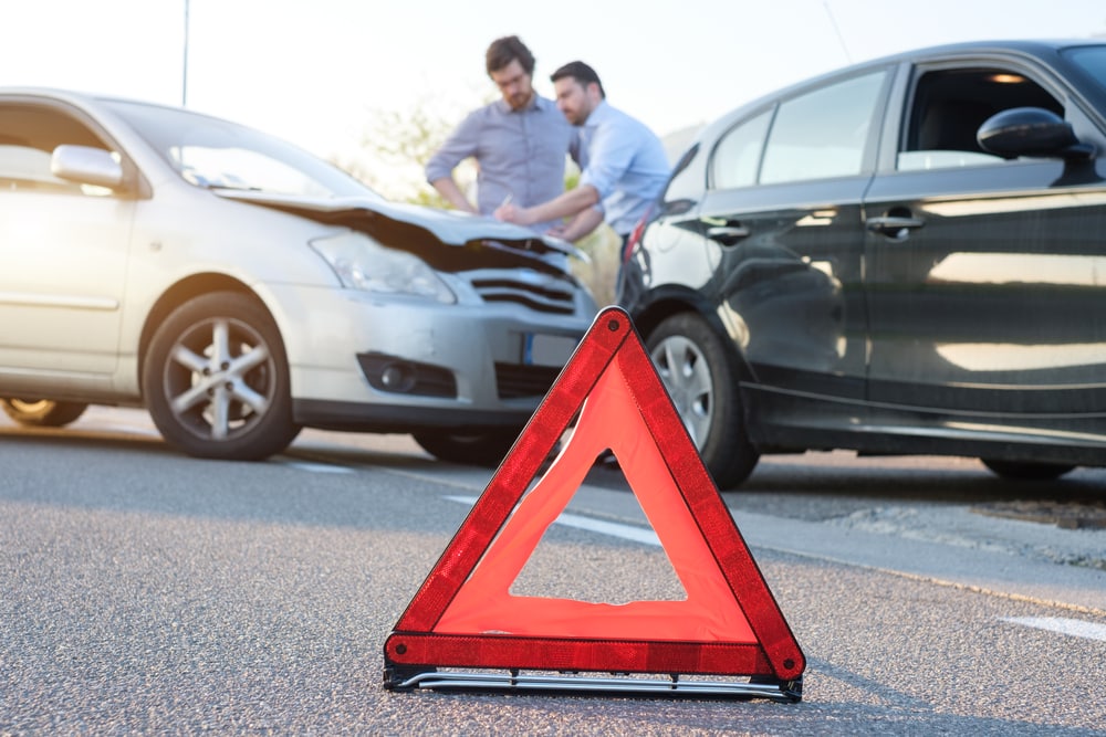emergency sign with a car accident with two men with collision insurance in california in the back