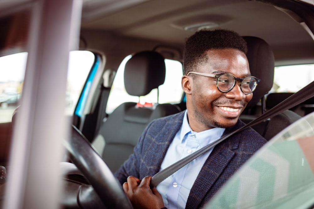 smiling african american man putting on seatbelt in drivers seat