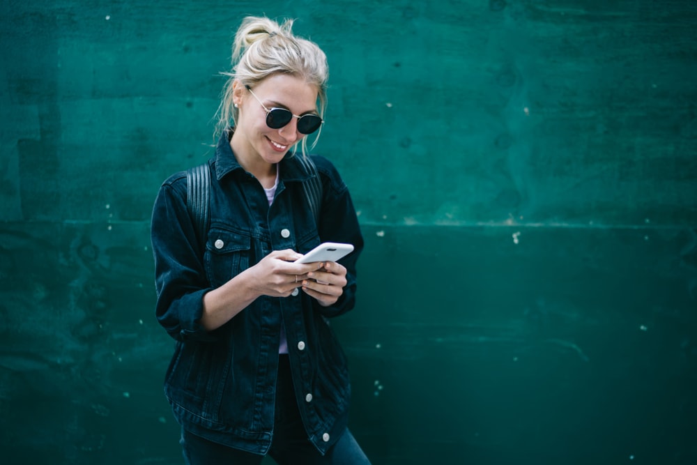 smiling young woman looking at phone for cheap car insurance