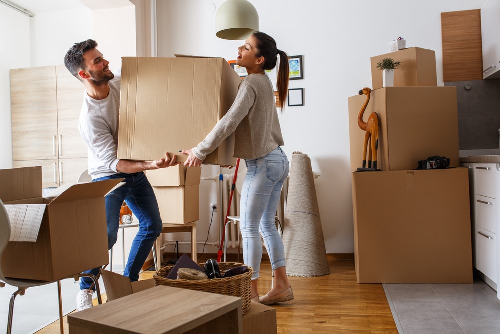 Young couple carrying big cardboard box at new home