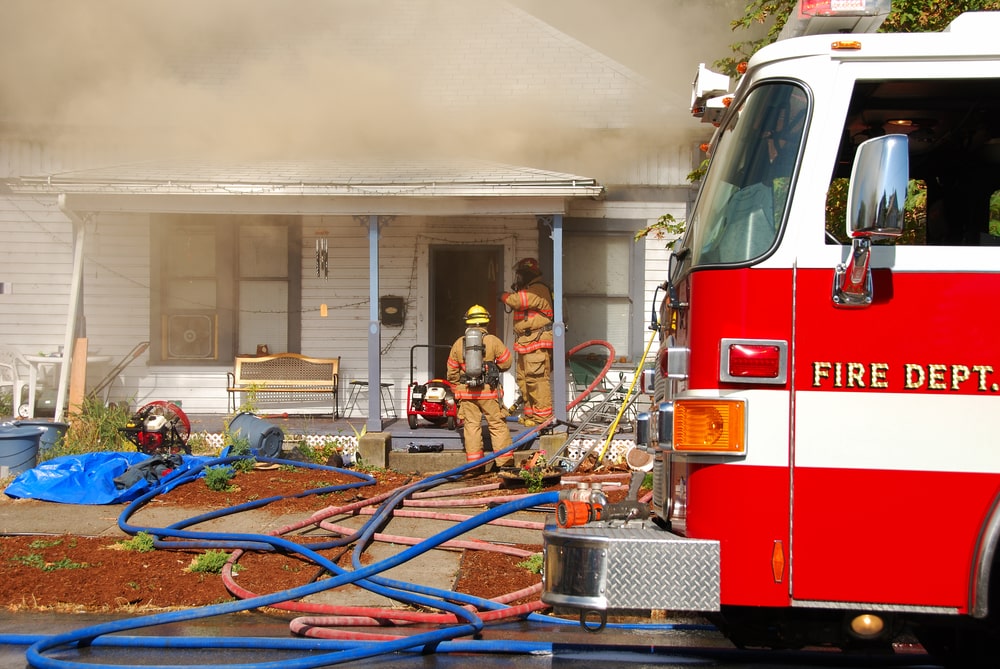 fire truck with burning home and fire fighters in the background