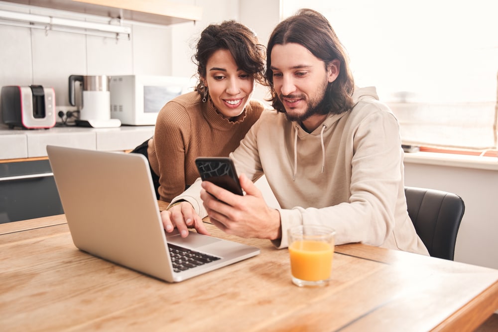 happy couple in kitchen with laptop looking for life insurance