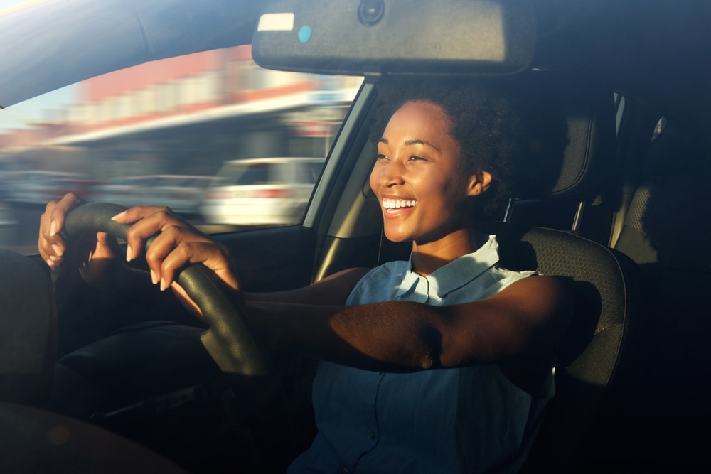 african american woman driving car with hands on the steering wheel smiling