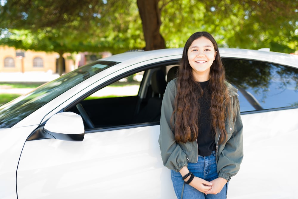 young teenage driver standing out front of her car