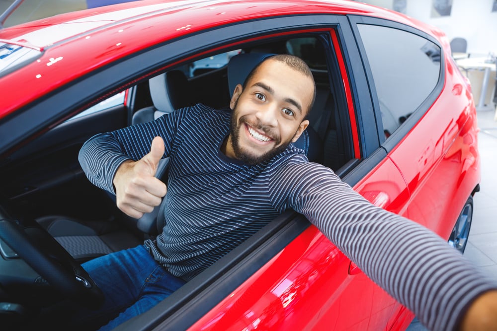 man smiling in drivers seat of red car