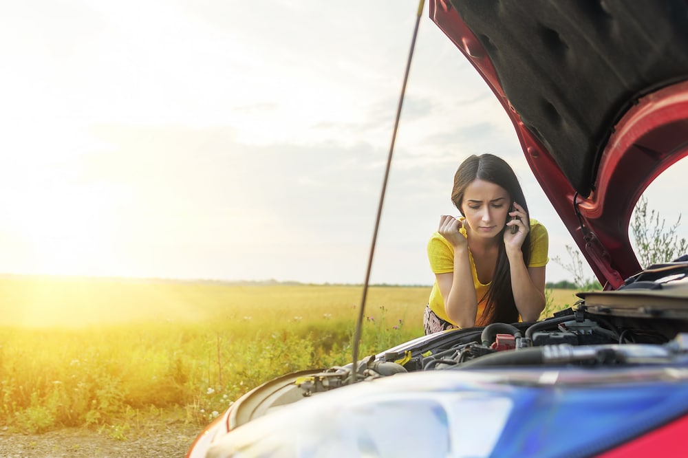 woman standing by car calling roadside assistance with hood up