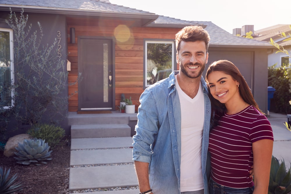 young couple standing outside of first home