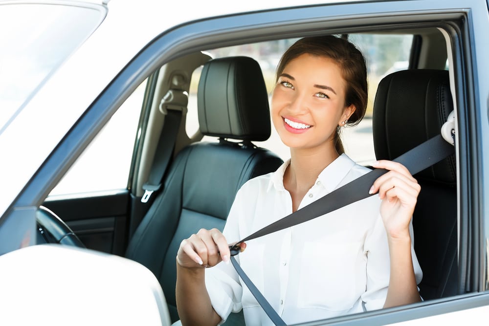 young female college driver smiling while buckling seat belt