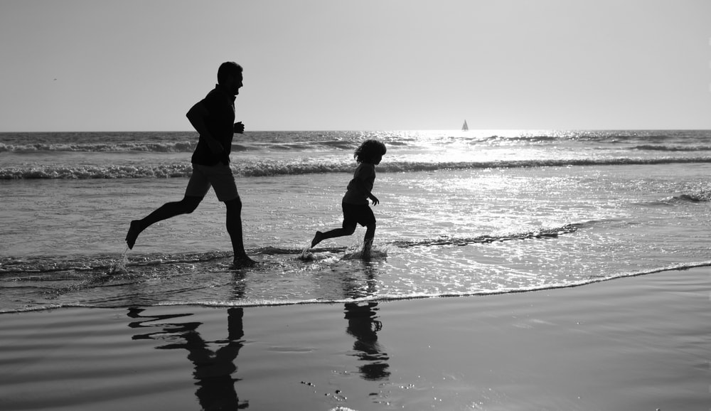 Man and child silhouette running on beach