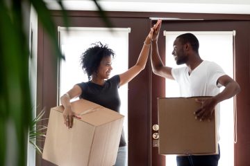 african american couple high fiving while moving into new apartment with boxes