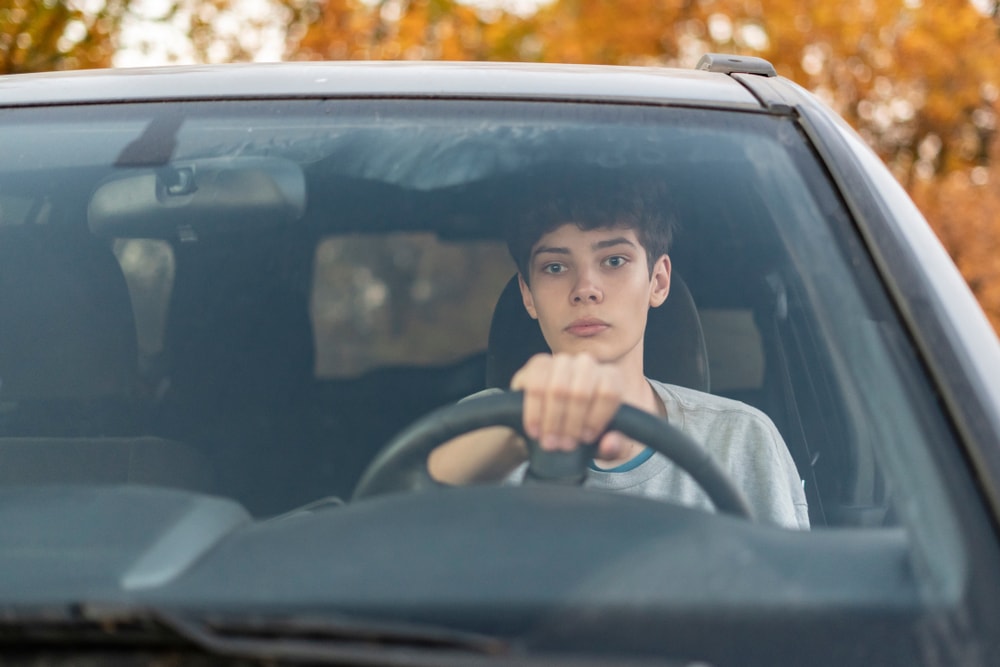 young teenage boy behind wheel of car