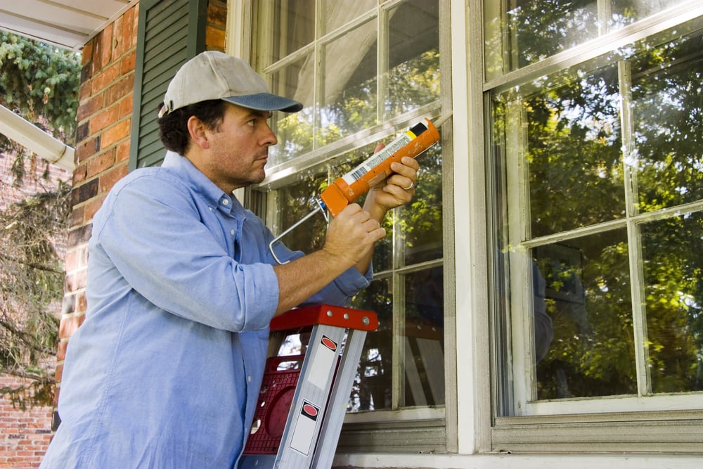 man sealing windows of home