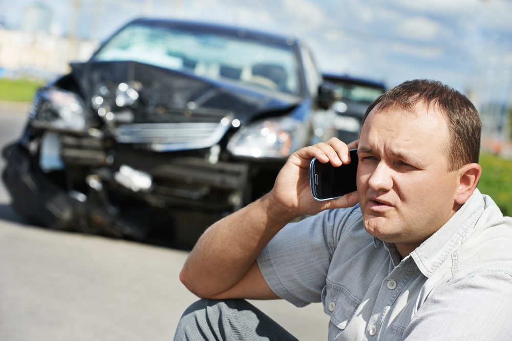 man on phone next to wrecked car