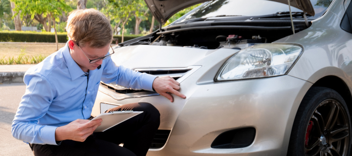 Insurance agent writing document on clipboard examining car after accident