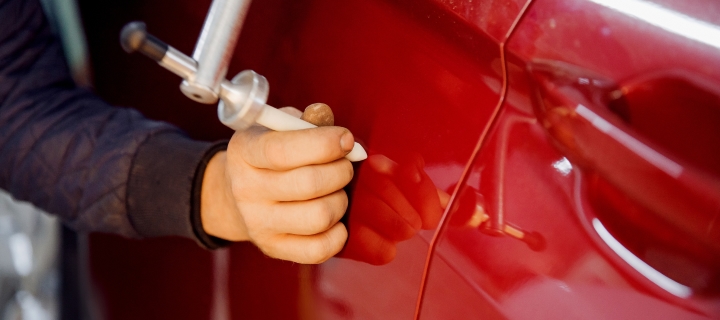 Person using pen to repair a dent on a red car