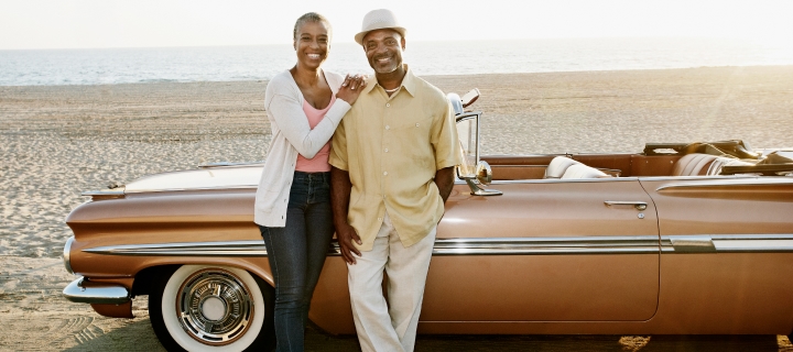 Elderly African American couple standing beside their classic car