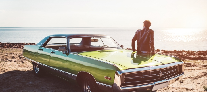 A man is standing near his green retro truck on the beach.