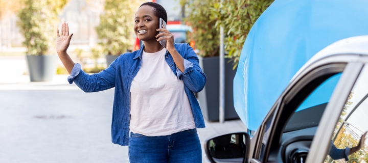 Cheerful young African American woman with car troubles calling for roadside assistance