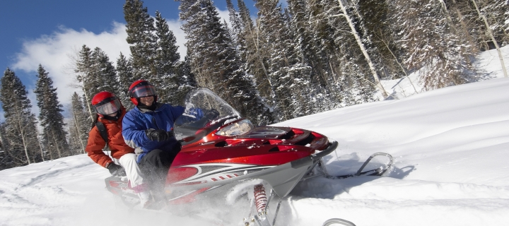 Couple driving snowmobile on snow covered track.