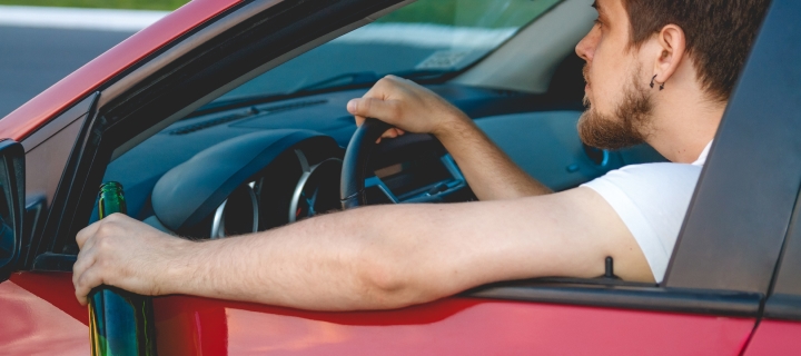 Young man driving with a bottle of beer.