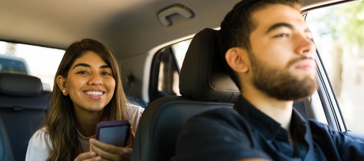 Happy lady sits in the back of a rideshare while the driver looks forward.