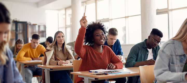 Happy African American student raising her hand to ask a question during lecture in the classroom.