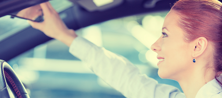 Happy young woman driver looking adjusting rear view car mirror, making sure line is free visibility is good before making turn. Human facial expressions, emotions. Safe trip, journey driving concept.
