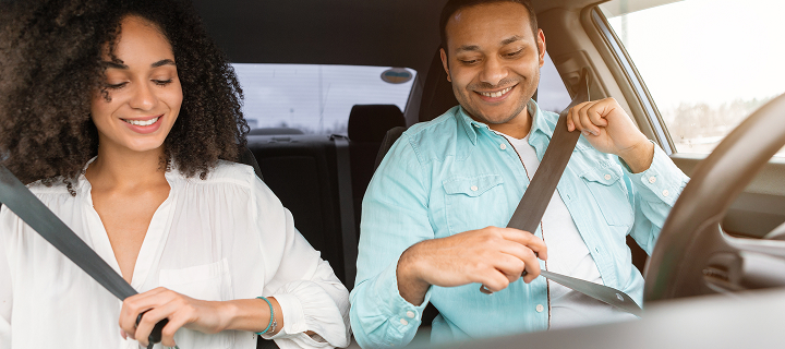 Road Safety Concept. African American couple practicing safe driving habits, wearing seat belts sitting in new car inside, enjoying comfort of vehicle.