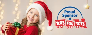 A smiling girl wearing a Santa hat and red sweater holds a wrapped gift in front of holiday lights next to text that reads “Proud Sponsor of Toys for Tots